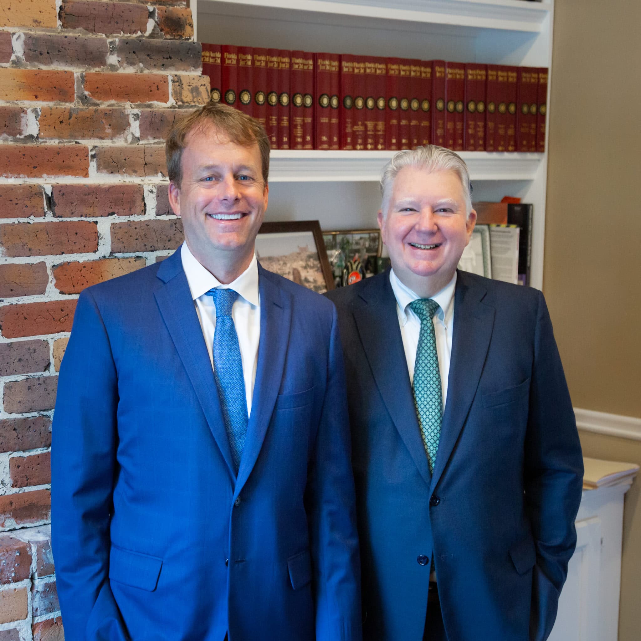 Two men in suits standing in front of a bookcase.