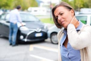 woman holding neck in pain with car accident in background