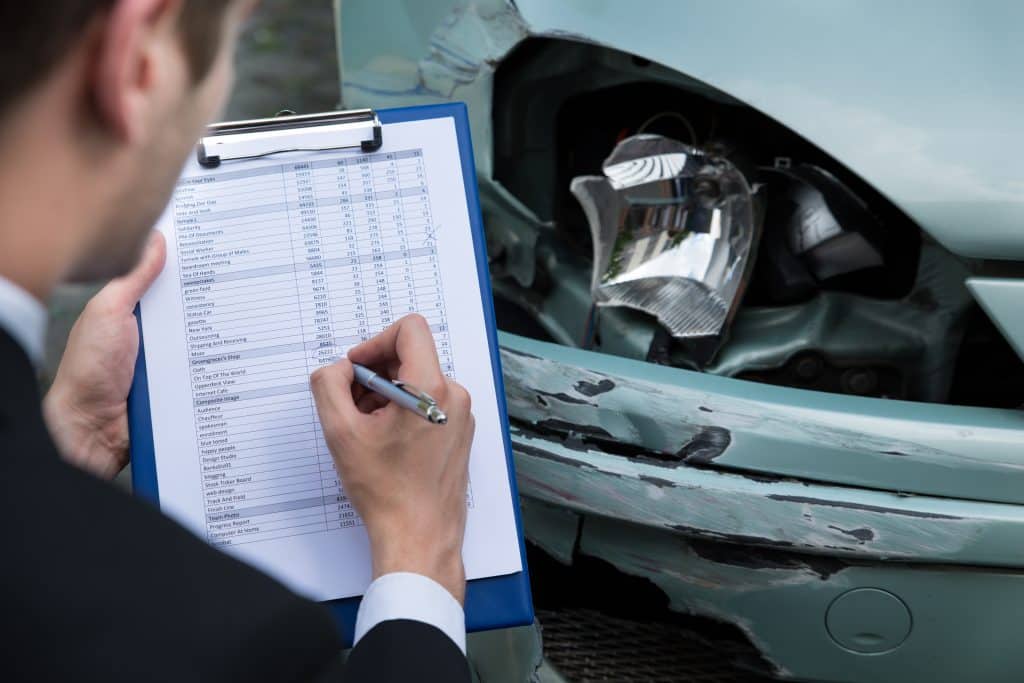 An insurance adjuster assesses the damage to a car after an accident
