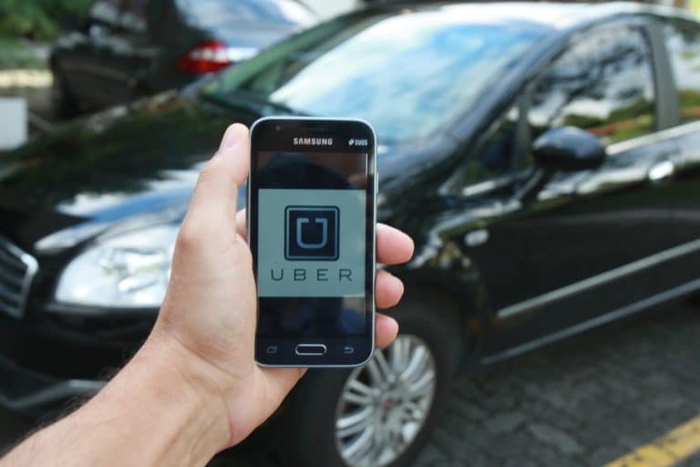 Hand holding phone in front of car with Uber logo displayed on screen