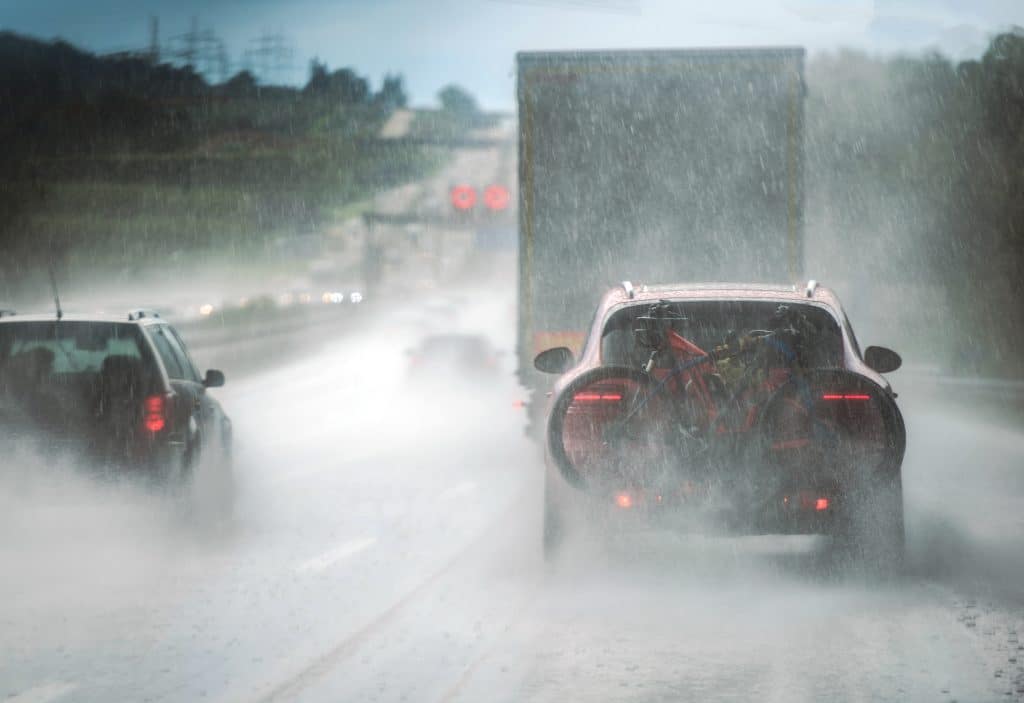 A car following a large commercial truck on a highway during a heavy rain.