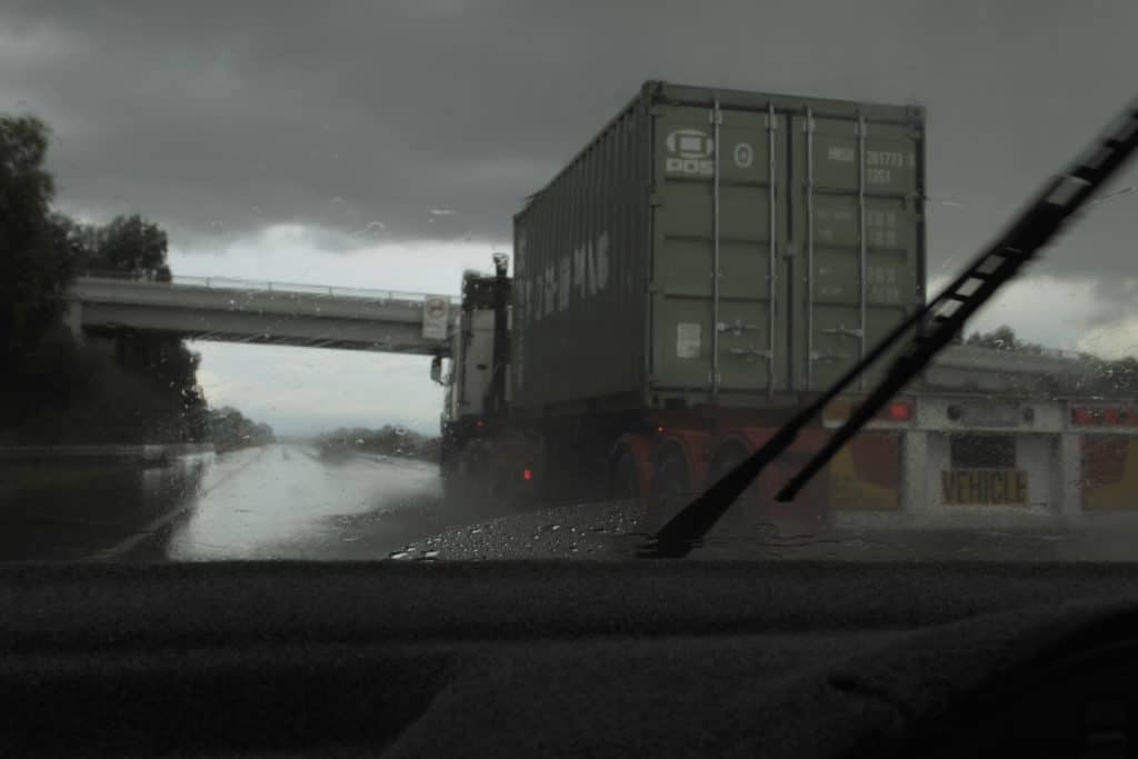 A view of a large commercial truck through a car's windshield on a rainy day.