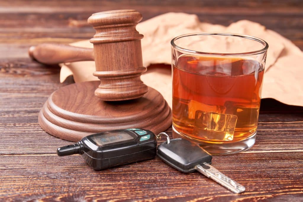 A glass of alcohol next to a judge's gavel and car keys
