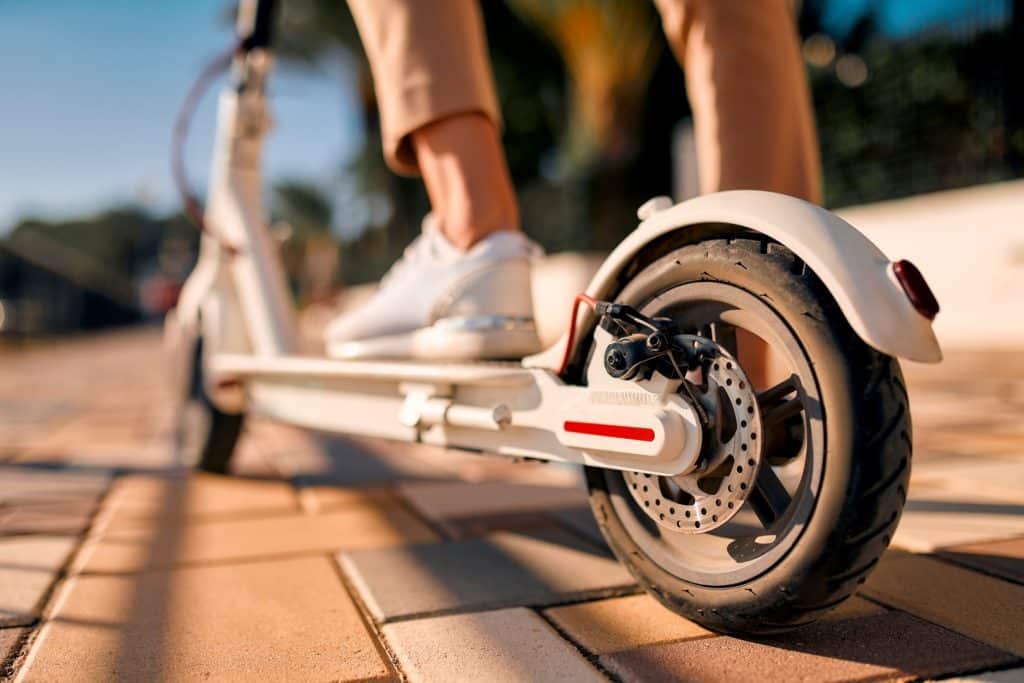 Close-up image of female feet on an electric scooter, with a wheel in the foreground.