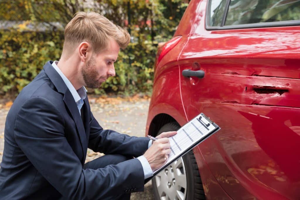Insurance Agent Writing On Clipboard While Examining Car After Accident
