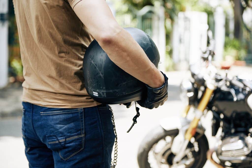 Man holding helmet under his arm with blurry motorcycle in background
