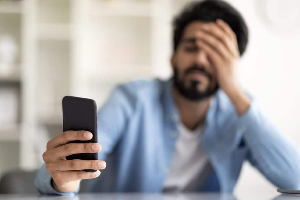 man holding phone while holding head in frustration