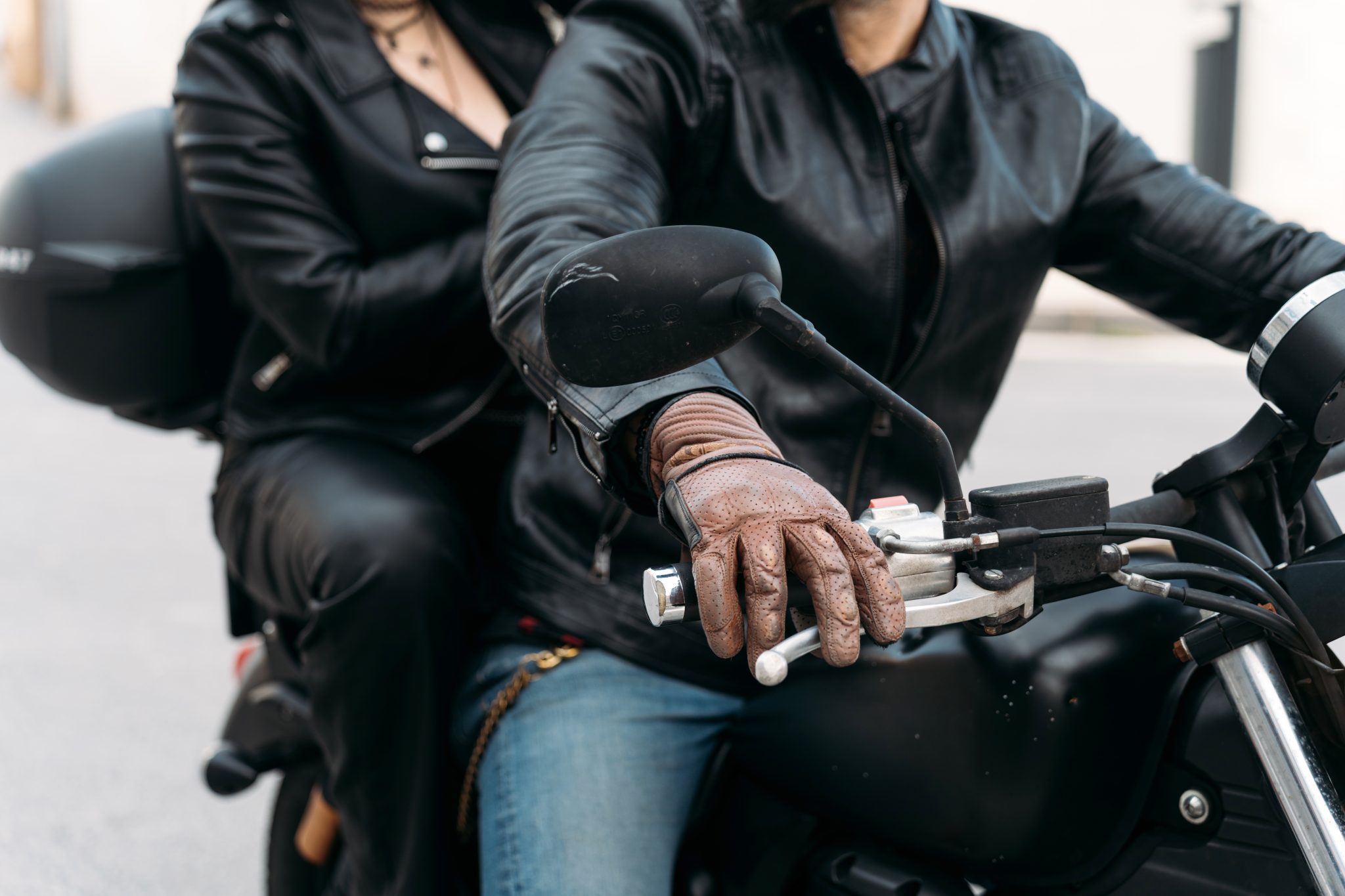 Bikers couple riding a motorcycle on the road, wearing leather jackets, brown leather gloves, and jeans
